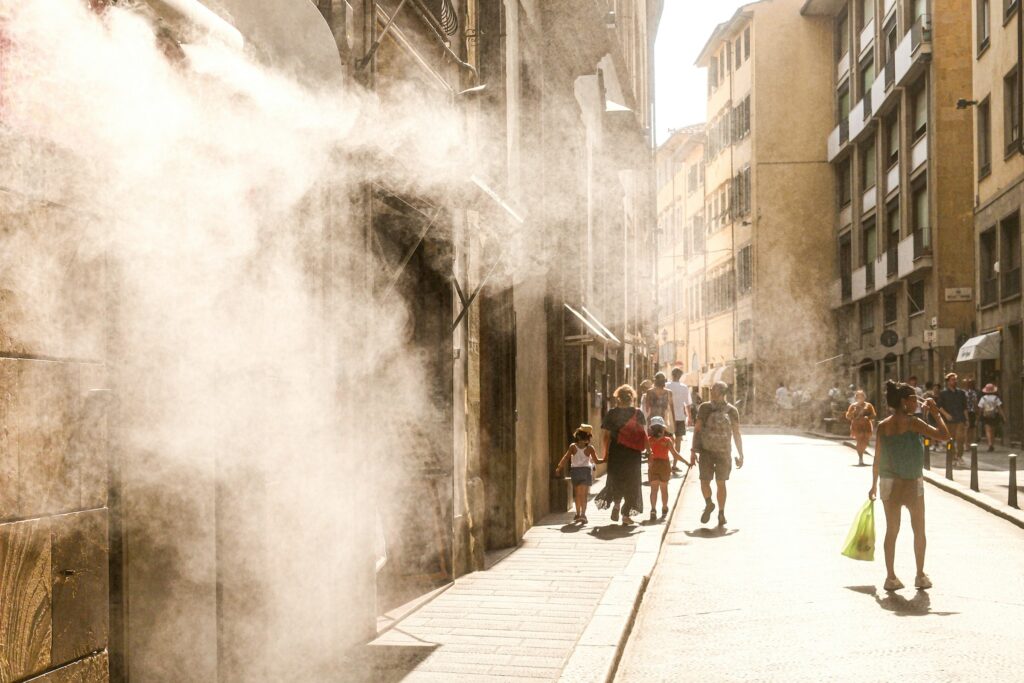 People walking along a sunny street with a water mist for cooling
