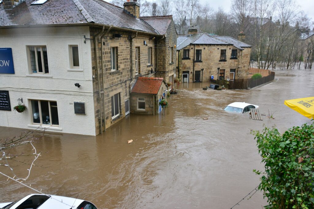 Floodwaters surrounding stone buildings and a partly submerged car in a town